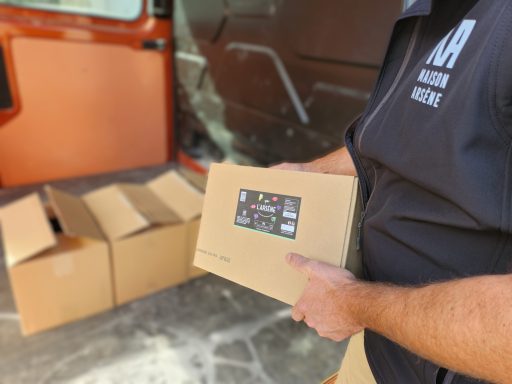 Un homme tient une boîte en carton, avec plusieurs autres boîtes à l'arrière d'un véhicule.