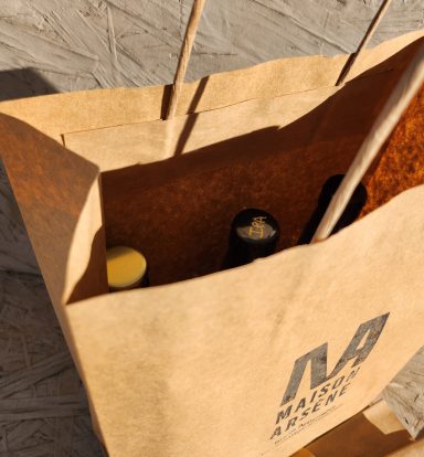 Sac en papier avec des bouteilles à l'intérieur, portant un logo sur le devant.